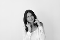 A smiling woman with flawless skin gently touching her cheek in a bright room.