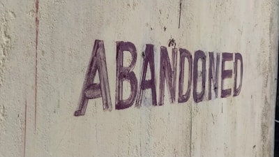 The word 'ABANDONED' is written in uppercase with dark, faded letters on a textured, weathered wall. The wall appears to be aged, with visible dirt and marks, suggesting neglect.