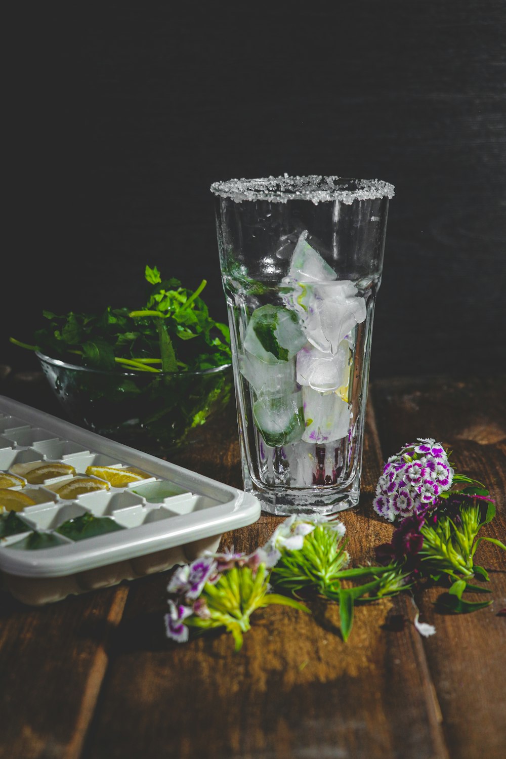 a glass filled with ice and flowers on a wooden table