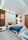 A modern bedroom with geometric wall panels and vibrant decor. The bed is adorned with colorful pillows and a blue blanket. Two pendant lights hang above each bedside table, enhancing the room's ambiance. Black and white photographs hang on the wall, and a textured rug lies on the floor.