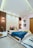 A modern bedroom with geometric wall panels and vibrant decor. The bed is adorned with colorful pillows and a blue blanket. Two pendant lights hang above each bedside table, enhancing the room's ambiance. Black and white photographs hang on the wall, and a textured rug lies on the floor.