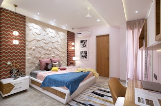 A modern bedroom features a bed with multicolored bedding, a 3D geometric wall design, and a patterned wallpaper. The room includes a white cabinet with drawers, elegant pendant lights, an air conditioner, and framed pictures on the wall. Floor-to-ceiling curtains enhance the room's soft lighting.