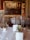 A formal dining room with round tables covered in white tablecloths, set with fine china, glasses, and menus. Elegant gold chairs surround the tables, and a large, ornate painting hangs on a rich, red-patterned wall. The room exudes a sense of classic elegance with its sophisticated decor.