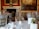 A luxurious dining room setting featuring elegantly arranged tables with white tablecloths, gold-colored chairs, and neatly placed tableware. The background showcases a grand fireplace with an ornate clock and large classical paintings adorning the walls.