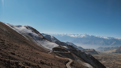 Snow-capped peaks of Ladakh under a clear blue sky, with a winding mountain road.