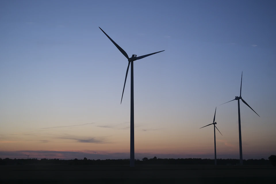 Three wind turbines stand tall against a serene sunset over a green field landscape