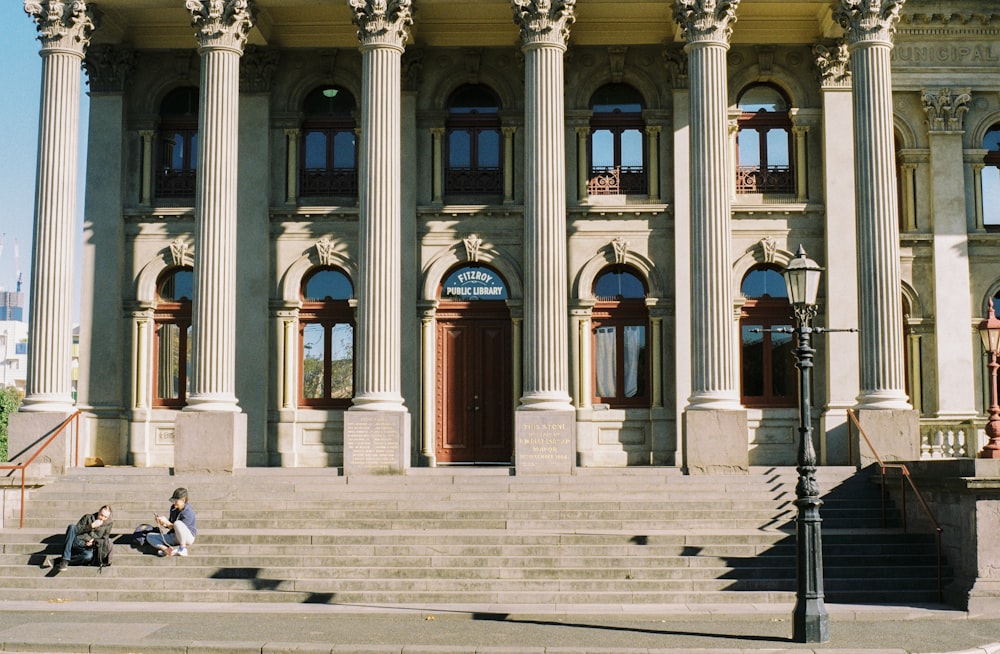 two people sitting on a bench in front of a building