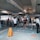 A busy subway or train station with multiple people walking through turnstiles. There is a sign indicating 'Taft Avenue' with directional arrows. A security guard is standing near a wet floor caution sign placed on the tiled floor. Several individuals are observed, some wearing face masks.