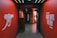 A hallway with vibrant red walls features motivational phrases such as 'Never Give Up' and 'Fight Until The End' in bold white lettering. On the left wall, there is an illustration of a cannon, symbolizing strength and resilience. The ceiling is adorned with several lines of light, creating an energetic atmosphere. At the end of the hallway, there is a doorway leading to a brighter area.