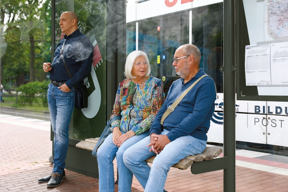 a man and woman sitting on a bench in front of a bus stop