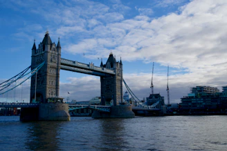 A modern suspension bridge spanning a wide river with construction cranes in the background.
