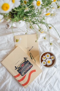 A vibrant flat lay of colorful journals and books with bright yellow, pink, purple, and green covers, surrounded by fresh flowers and a cup of tea.