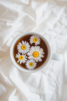 A cozy tea cup with rising steam surrounded by tea leaves and soft ivory background.
