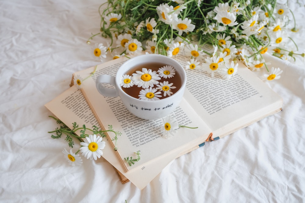 a cup of tea and some daisies on a book