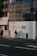 Two construction workers wearing safety helmets are walking near a construction site under warm, late afternoon light. The building exterior is covered with signage related to sustainable development goals and a temporary uniform wall enclosing the site.