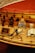 A detailed model of a wooden ship's deck, featuring coiled ropes, wooden barrels, and a well-crafted anchor. There are also bundles of sacks and various nautical elements placed on the realistic-looking planks.