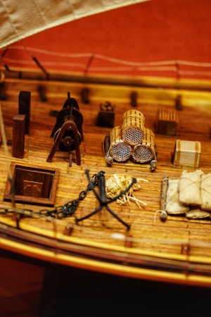 A detailed model of a wooden ship's deck, featuring coiled ropes, wooden barrels, and a well-crafted anchor. There are also bundles of sacks and various nautical elements placed on the realistic-looking planks.