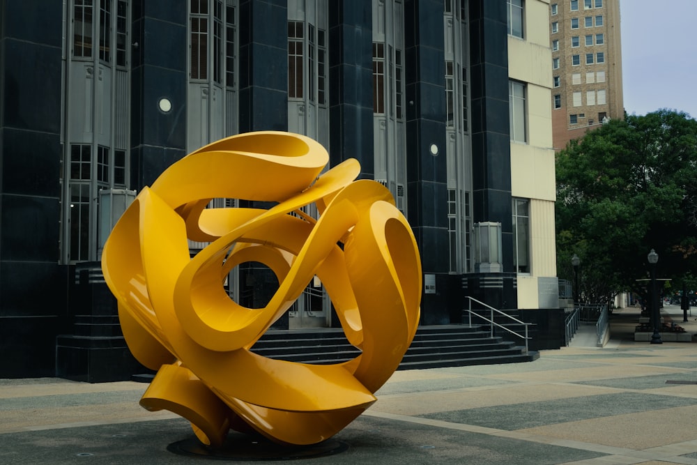 a large yellow sculpture sitting in front of a tall building