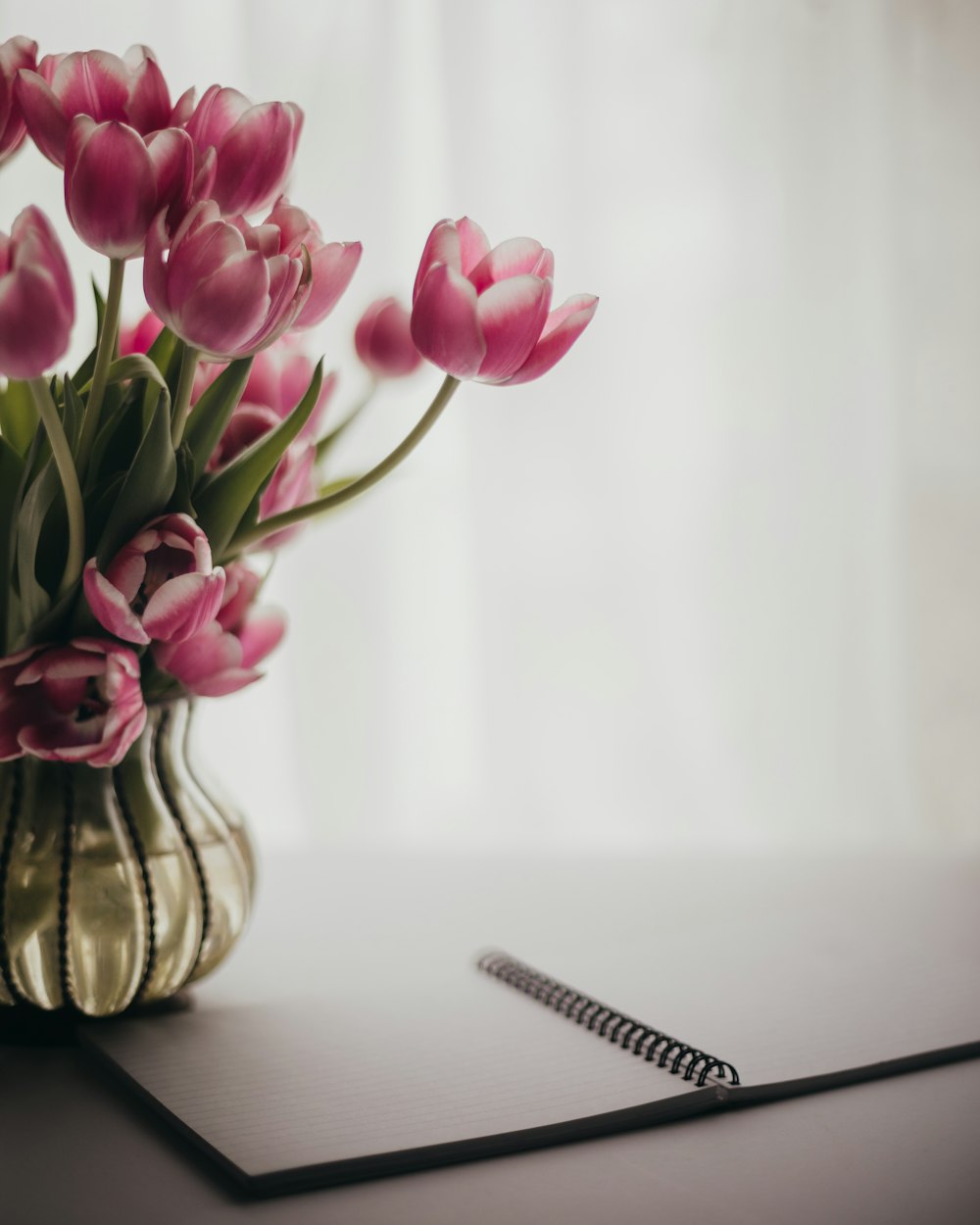 Un jarrón lleno de tulipanes rosados sentado encima de una mesa