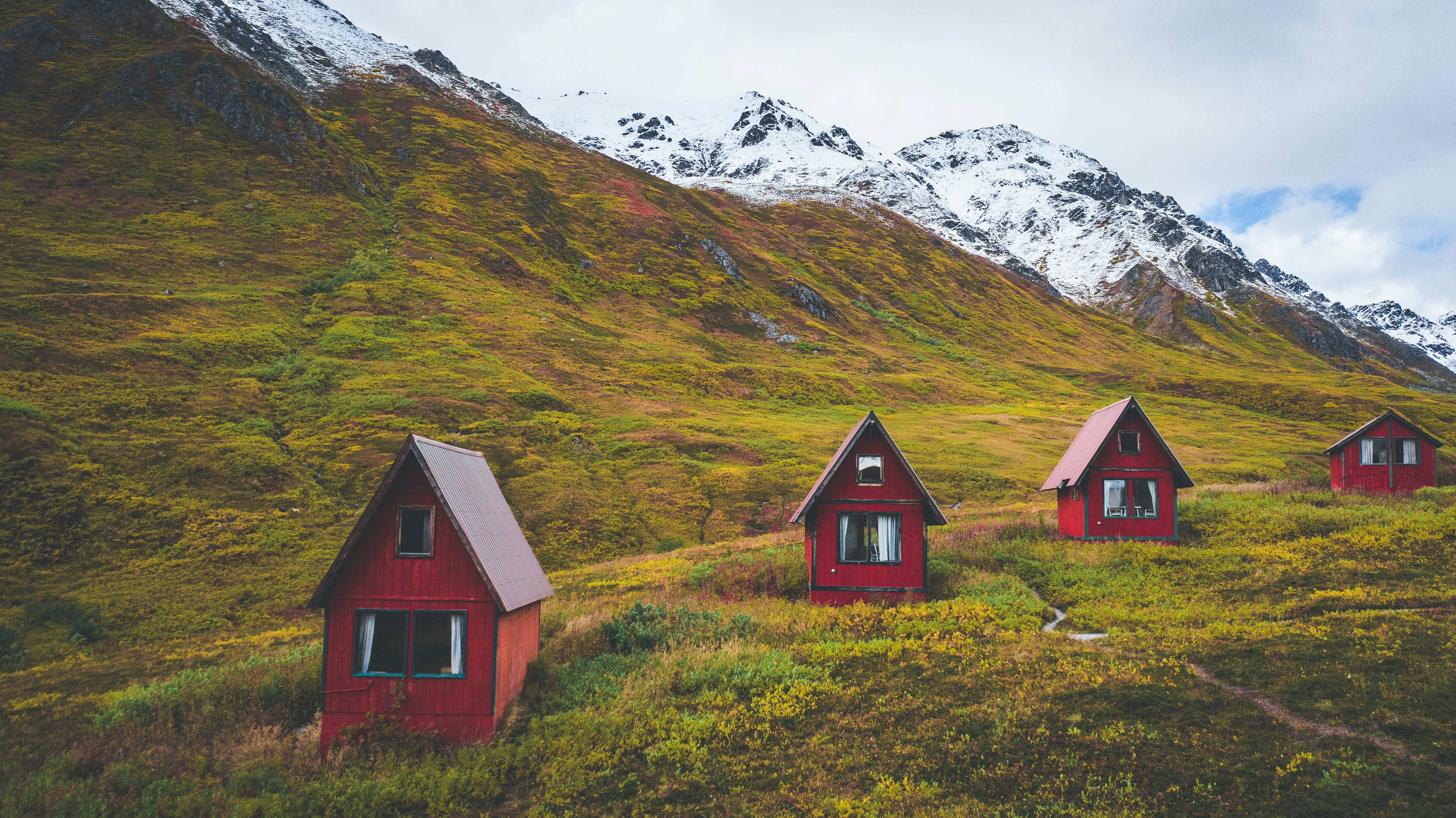 a group of red cabins sitting on top of a lush green hillside, Drone view of cabins during peak foliage in Hatcher Pass, Alaska.