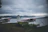 Man standing beside a floatplane on a remote Alaskan lake, mountains in the background.
