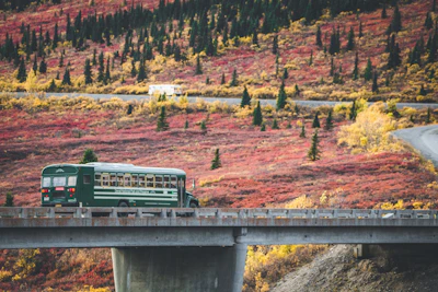 a green bus driving over a bridge in the mountains