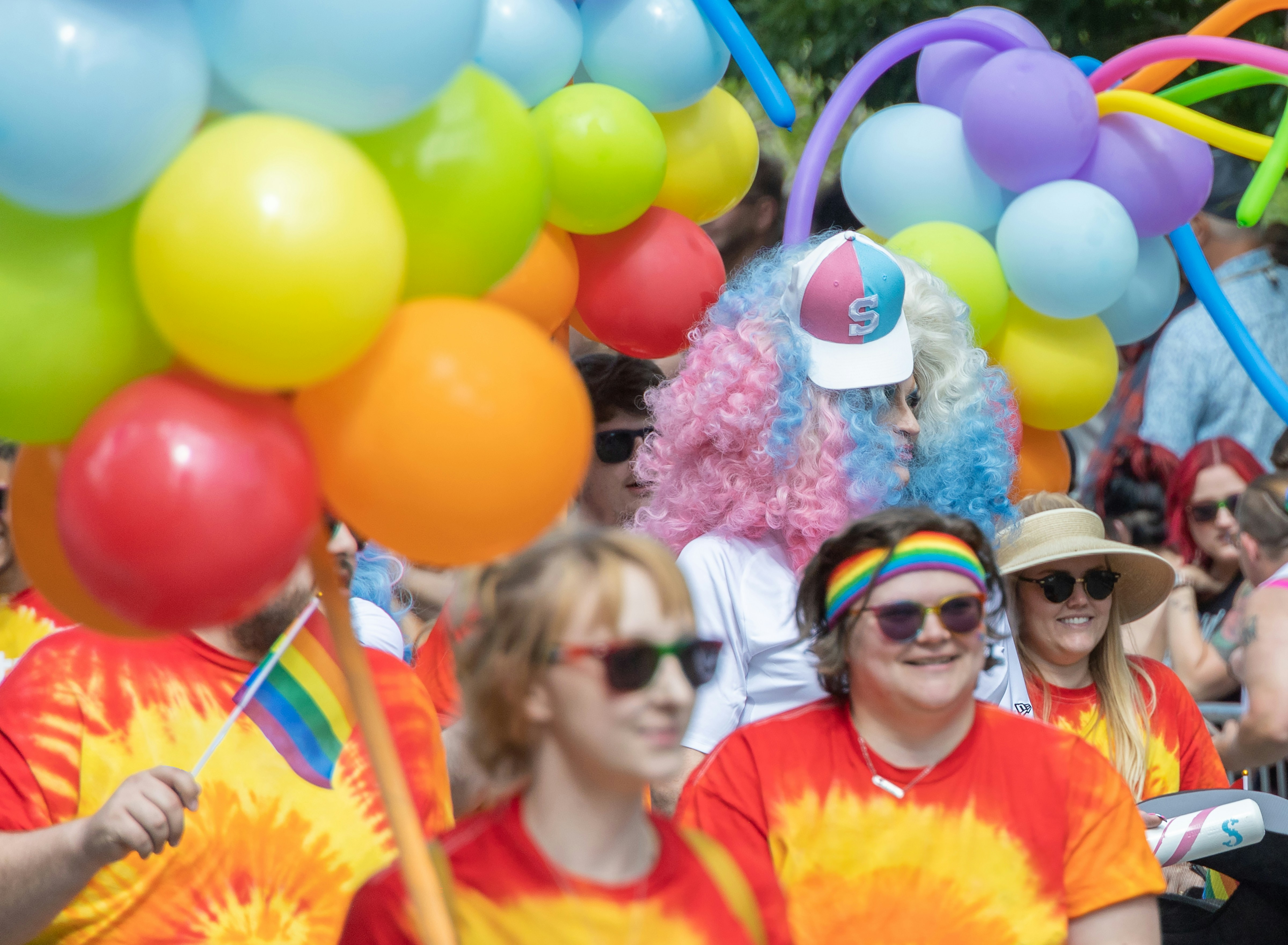 Forskelligartet gruppe fejrer udendørs med farverige balloner og tie-dye t-shirts.