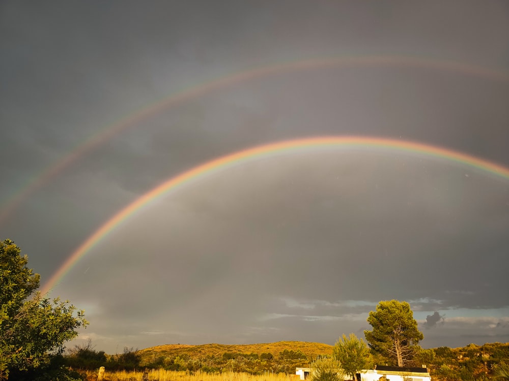 a double rainbow over a field with a house in the background