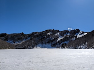 A wide shot of a frozen lake reflecting snowy peaks on a crisp winter day.