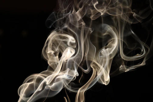 Abstract shot of swirling smoke illuminated by charcoal gray and gold lights, evoking mystery.