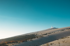 a hill covered in sand and trees under a blue sky
