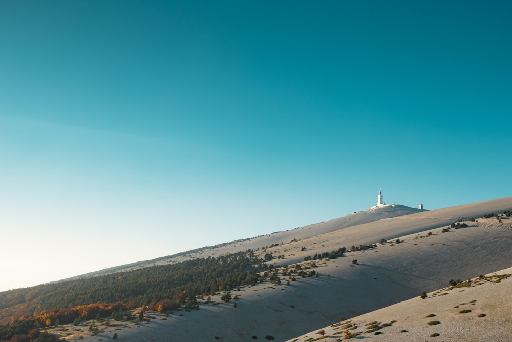 a hill covered in sand and trees under a blue sky