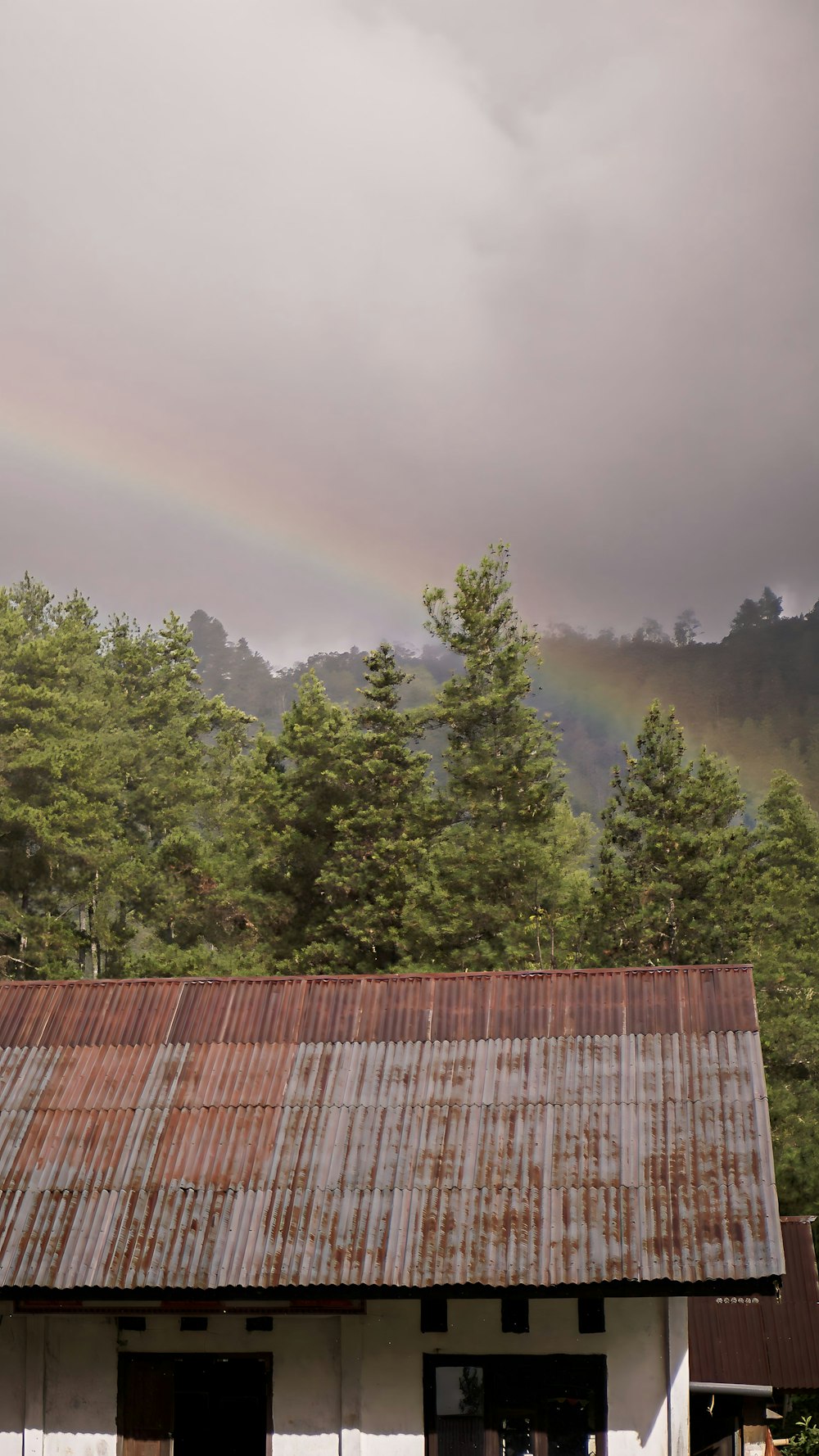 a building with a rusted tin roof and a rainbow in the background