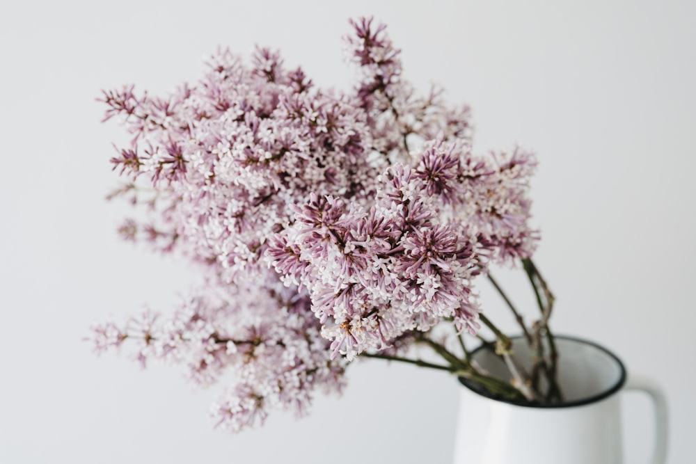 a white vase filled with purple flowers on top of a table