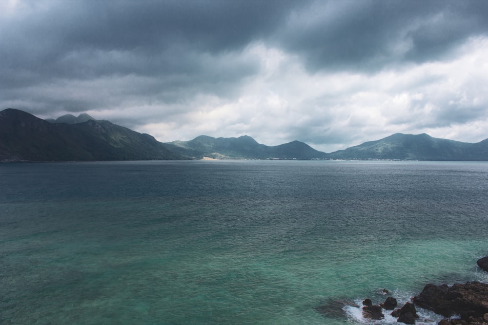 a body of water surrounded by mountains under a cloudy sky