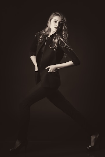 A sleek model wearing a monochrome tailored blazer and wide-leg trousers, standing confidently against a minimalist urban backdrop.