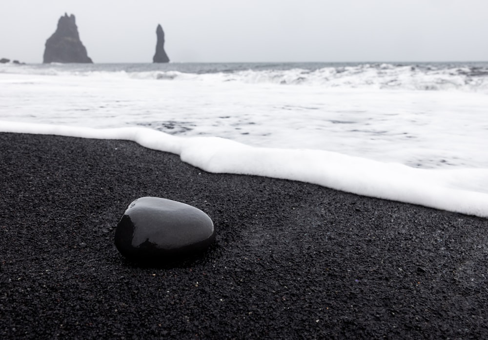 a rock sitting on top of a black sand beach