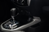 An interior view of a car's dashboard featuring an automatic gear shift lever. The gear shift is metallic with a black handle, and the panel includes a USB port. Surrounding controls for the vehicle's air conditioning system and power outlets can be seen.