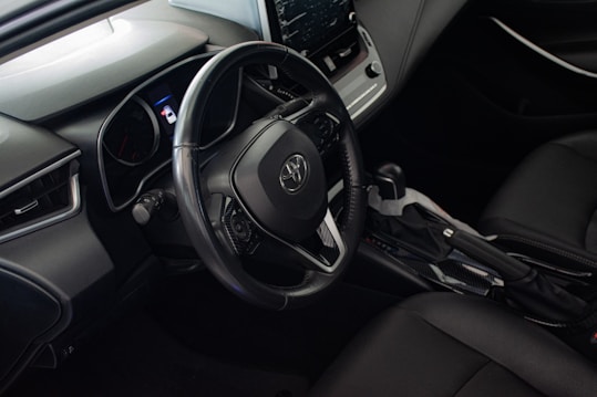 A car's interior focusing on the steering wheel, dashboard, and center console. The design appears modern with a combination of dark materials and chrome accents.