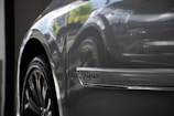 Close-up of a car's side, focusing on the wheel and a chrome emblem with the word 'Corolla.' The car surface has a glossy finish, reflecting light and the surrounding environment.