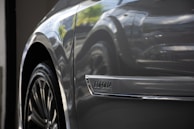 Close-up of a car's side, focusing on the wheel and a chrome emblem with the word 'Corolla.' The car surface has a glossy finish, reflecting light and the surrounding environment.