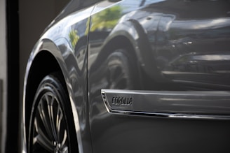 Close-up of a car's side, focusing on the wheel and a chrome emblem with the word 'Corolla.' The car surface has a glossy finish, reflecting light and the surrounding environment.