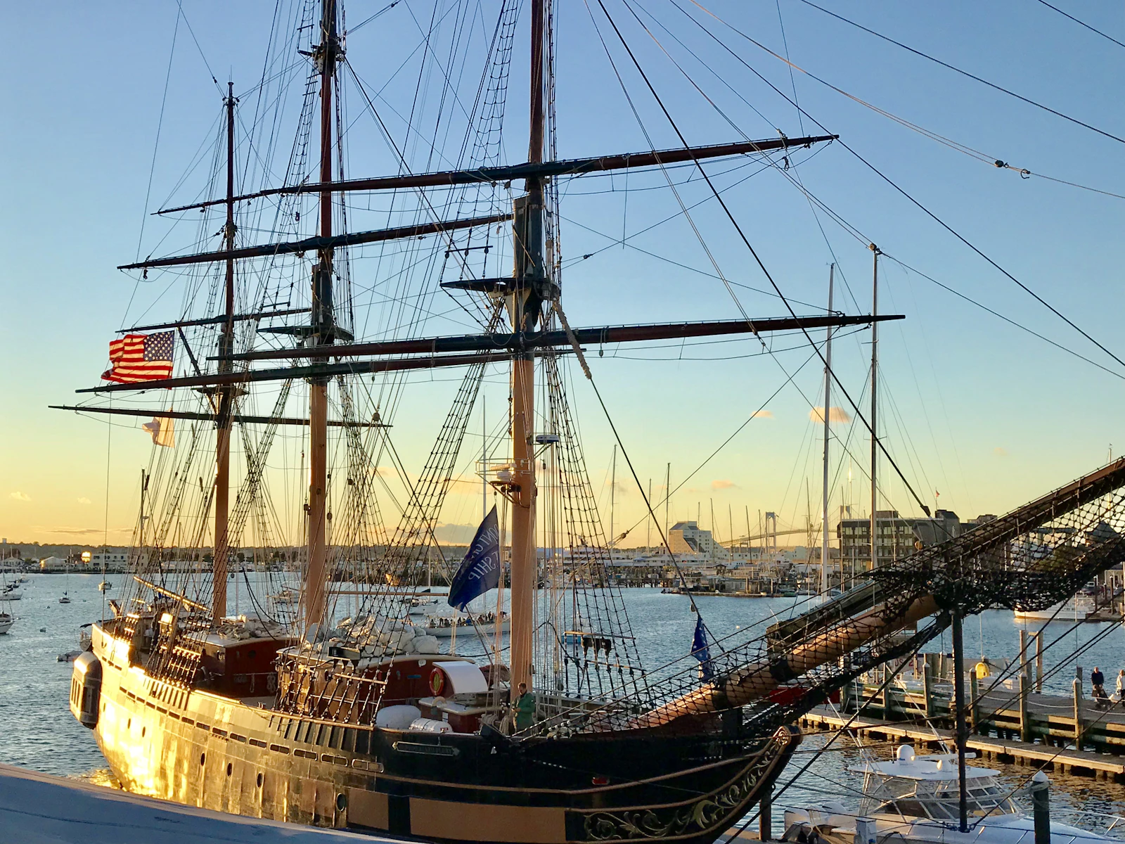 A tall ship at a New England pier at golden hour with an American flag flying