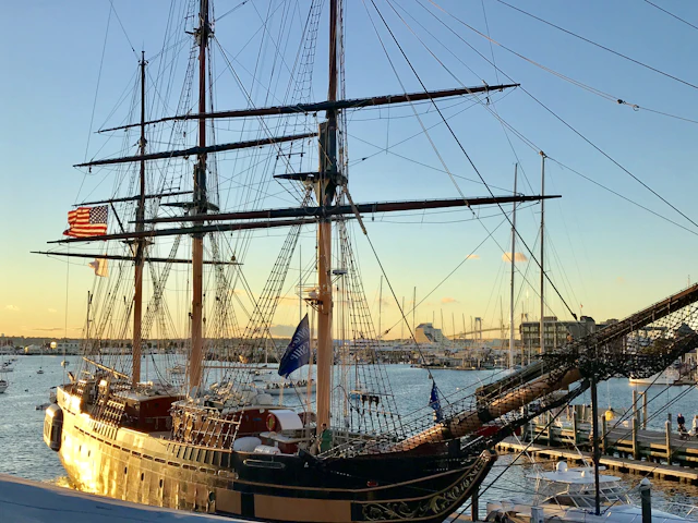 A tall ship at a New England pier at golden hour with an American flag flying