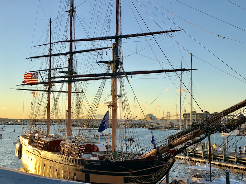 A tall ship at a New England pier at golden hour with an American flag flying