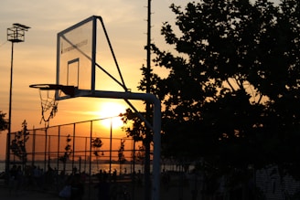 A vibrant basketball court at sunset with players practicing and fans watching nearby.