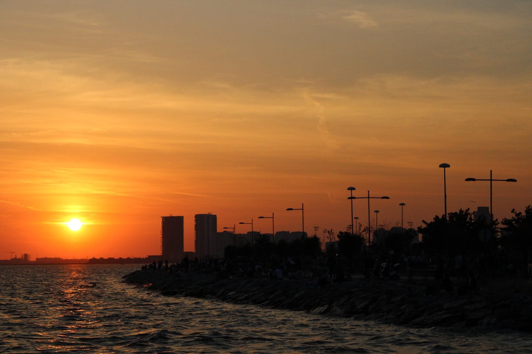 a sunset over a body of water with a city in the background, Sunset in city coast