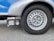 A close-up view of a silver vehicle wheel with a circular design featuring multiple holes around the rim. Adjacent to the wheel is a device labeled 'Truma Mover XT', which is likely a motorized mover for the vehicle. The surface is asphalt and the vehicle body is visible in shades of silver and blue.