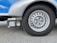 A close-up view of a silver vehicle wheel with a circular design featuring multiple holes around the rim. Adjacent to the wheel is a device labeled 'Truma Mover XT', which is likely a motorized mover for the vehicle. The surface is asphalt and the vehicle body is visible in shades of silver and blue.
