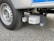 A close-up view of a vehicle wheel on a textured asphalt surface, featuring a Truma Mover XT device attached near the tire. The tire tread and the mechanical components of the mover stand out prominently.